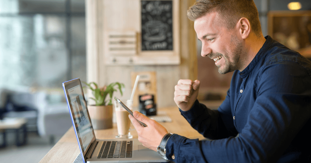 Ragazzo che guarda il suo computer e il suo telefono sorridendo perché ha trovato lavoro su LinkedIn